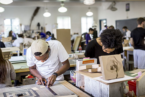 Students grin as they lean over their work in the lsu architecture studios